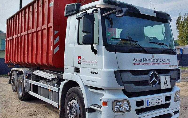 Container-Lkw des Unternehmens beim Absetzen eines roten Containers